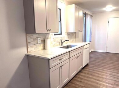 Kitchen with backsplash, dark wood finished floors, light stone counters, and white dishwasher