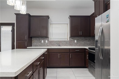 Kitchen featuring appliances with stainless steel finishes, light tile patterned floors, tasteful backsplash, dark brown cabinetry, and a kitchen island