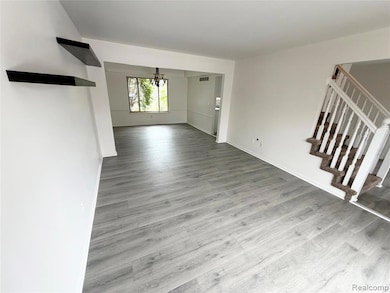 Unfurnished living room with stairway, light wood-style flooring, and a chandelier