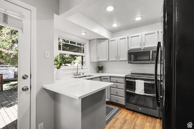 Kitchen featuring black appliances, light wood-style floors, recessed lighting, a peninsula, and light stone countertops