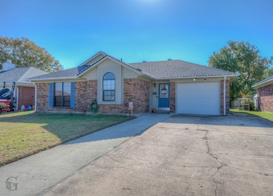 Ranch-style home featuring a front yard, concrete driveway, brick siding, roof with shingles, and an attached garage