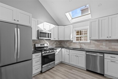 Kitchen with stainless steel appliances, white cabinets, dark stone counters, backsplash, and high vaulted ceiling