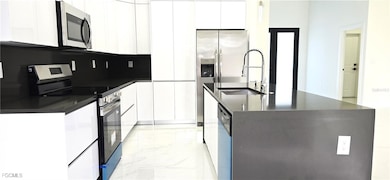 Kitchen with stainless steel appliances, light marble finish flooring, an island with sink, dark stone countertops, and white cabinets