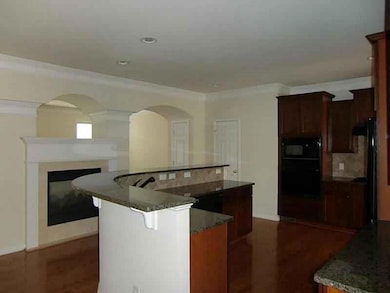 Kitchen featuring crown molding, an island with sink, dark stone counters, a breakfast bar area, and black appliances