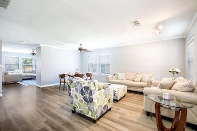 Living room featuring ceiling fan, crown molding, a textured ceiling, and wood finished floors
