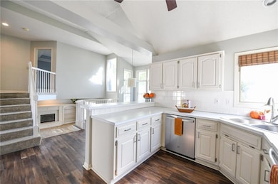 Kitchen featuring a peninsula, dishwasher, white cabinetry, vaulted ceiling, and light countertops