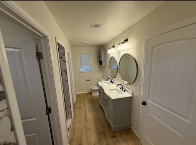 Full bath with toilet, wood finished floors, double vanity, and baseboards