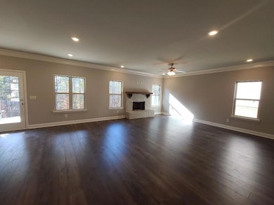 Unfurnished living room featuring crown molding, ceiling fan, dark wood-style flooring, a fireplace with raised hearth, and recessed lighting