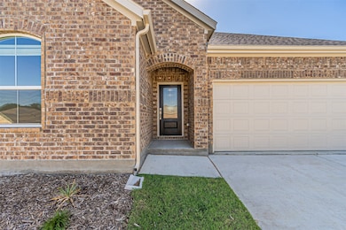 View of exterior entry featuring brick siding, driveway, an attached garage, and a shingled roof