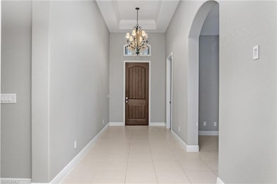 Entryway featuring light tile patterned flooring, a chandelier, arched walkways, a raised ceiling, and crown molding