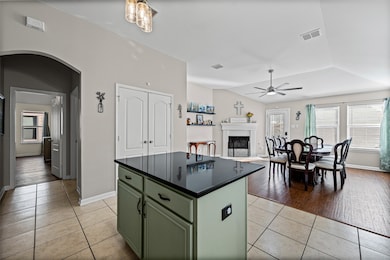 Kitchen featuring green cabinetry, light tile patterned floors, a center island, a fireplace, and arched walkways