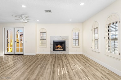 Unfurnished living room with a textured ceiling, recessed lighting, a high end fireplace, light wood-type flooring, and ceiling fan