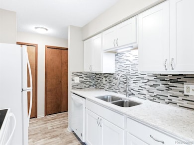 Kitchen featuring white cabinetry, white appliances, decorative backsplash, light stone counters, and light wood-style flooring