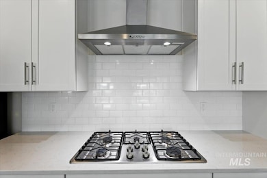 Kitchen featuring wall chimney exhaust hood, stainless steel gas cooktop, white cabinetry, backsplash, and light stone countertops