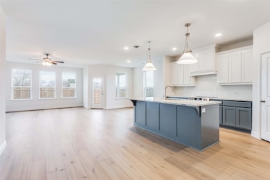 Kitchen with sink, white cabinets, hanging light fixtures, a center island with sink, and light wood-type flooring