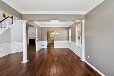 Unfurnished dining area with ornate columns, dark wood-style flooring, crown molding, stairway, and a chandelier