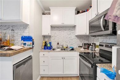Kitchen with stainless steel appliances, backsplash, ornamental molding, white cabinets, and light wood-type flooring