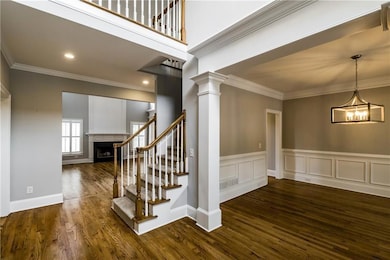 Stairs with a fireplace, wood finished floors, crown molding, a chandelier, and ornate columns