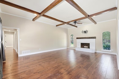 Unfurnished living room featuring dark wood floors, coffered ceiling, beamed ceiling, and a brick fireplace