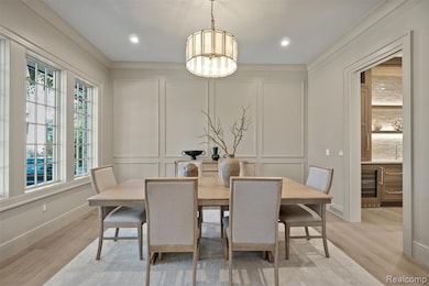 Dining space featuring a decorative wall, beverage cooler, light wood-style flooring, and ornamental molding