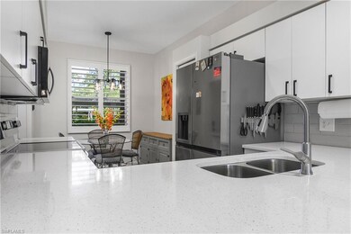 Kitchen with stainless steel appliances, hanging light fixtures, white cabinetry, decorative backsplash, and light stone countertops
