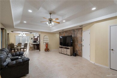 Living room with a tray ceiling, a textured ceiling, a chandelier, a ceiling fan, and recessed lighting