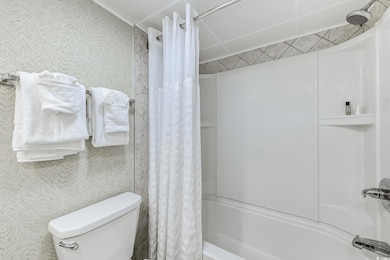 Bathroom with wallpapered walls, shower / bath combo with shower curtain, and toilet