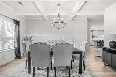 Dining space featuring a chandelier, light wood finished floors, beamed ceiling, coffered ceiling, and crown molding