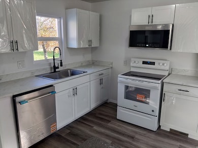 Kitchen with appliances with stainless steel finishes, white cabinetry, and dark wood-style floors