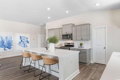 Kitchen with gray cabinetry, appliances with stainless steel finishes, dark wood-style floors, a center island with sink, and a breakfast bar area