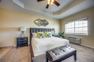 Carpeted bedroom with a raised ceiling, a wall mounted AC, and ceiling fan