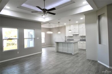 Kitchen with white cabinetry, a tray ceiling, ceiling fan with notable chandelier, pendant lighting, and hardwood / wood-style floors