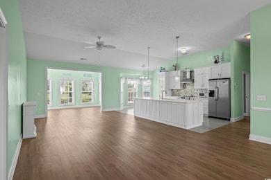 Unfurnished living room featuring a ceiling fan, light wood finished floors, baseboards, a textured ceiling, and a chandelier