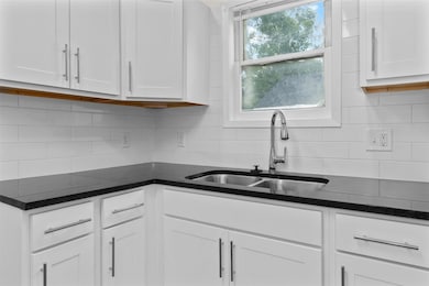 Kitchen with white cabinets, decorative backsplash, and dark stone counters