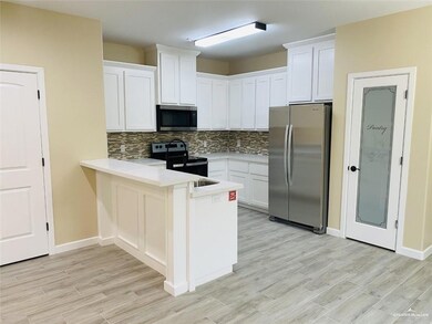 Kitchen featuring decorative backsplash, appliances with stainless steel finishes, a peninsula, light countertops, and white cabinetry