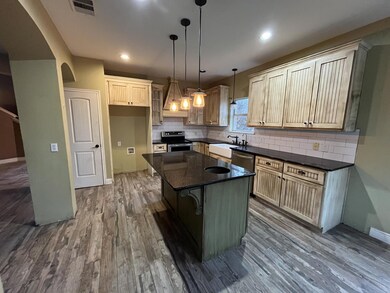 Kitchen featuring a center island, dark stone countertops, stainless steel electric range oven, green cabinetry, and pendant lighting