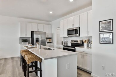 Kitchen with stainless steel appliances, tasteful backsplash, white cabinetry, light stone counters, and a kitchen bar