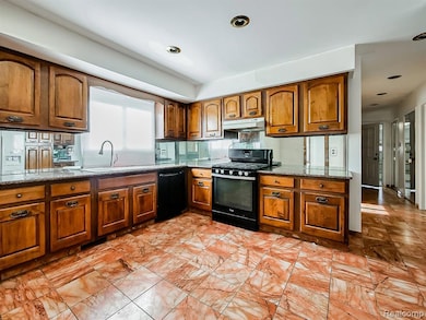 Kitchen with brown cabinetry, dark stone counters, black appliances, and under cabinet range hood