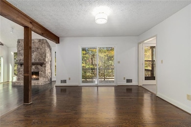 Spare room with a stone fireplace, dark wood-style flooring, and a textured ceiling
