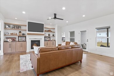 Living room with light wood finished floors, visible vents, a glass covered fireplace, recessed lighting, and a ceiling fan