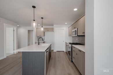Kitchen with appliances with stainless steel finishes, pendant lighting, a kitchen island with sink, light wood finished floors, and decorative backsplash