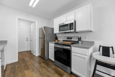 Kitchen featuring stainless steel appliances, white cabinets, dark wood finished floors, and light countertops