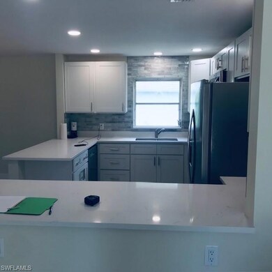 Kitchen featuring freestanding refrigerator, a peninsula, white cabinets, light stone counters, and backsplash
