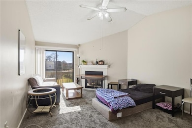 Living room featuring a textured ceiling, a fireplace, carpet, lofted ceiling, and ceiling fan