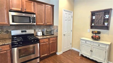 Kitchen featuring appliances with stainless steel finishes, dark wood-style floors, decorative backsplash, baseboards, and dark stone counters