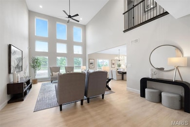 Living area featuring light wood-type flooring, a high ceiling, a ceiling fan, and a chandelier