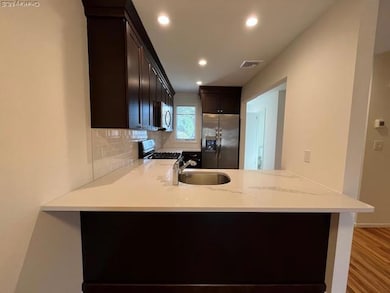 Kitchen featuring light stone counters, appliances with stainless steel finishes, backsplash, a peninsula, and dark brown cabinetry