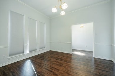 Empty room with dark wood-type flooring, ornamental molding, and a chandelier