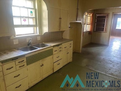 Kitchen featuring unfinished concrete floors, tile countertops, tasteful backsplash, arched walkways, and wooden walls