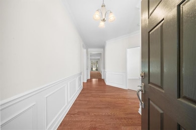 Corridor featuring crown molding, a chandelier, wainscoting, a decorative wall, and wood finished floors